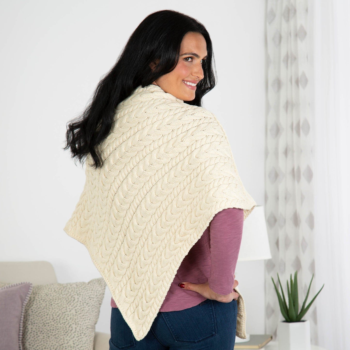 Woman wearing a cream-colored knitted poncho in a home setting