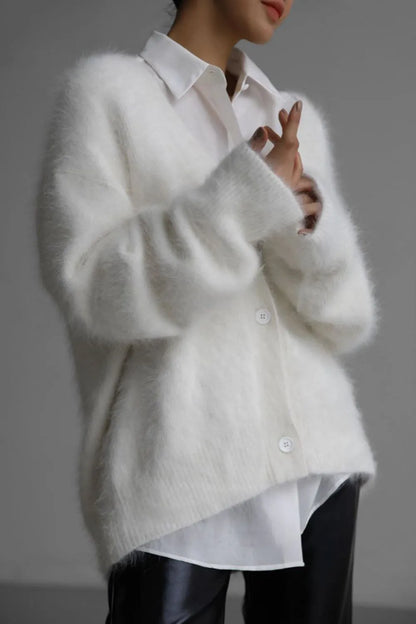 Person wearing a white textured sweater over a white shirt with a blurred background