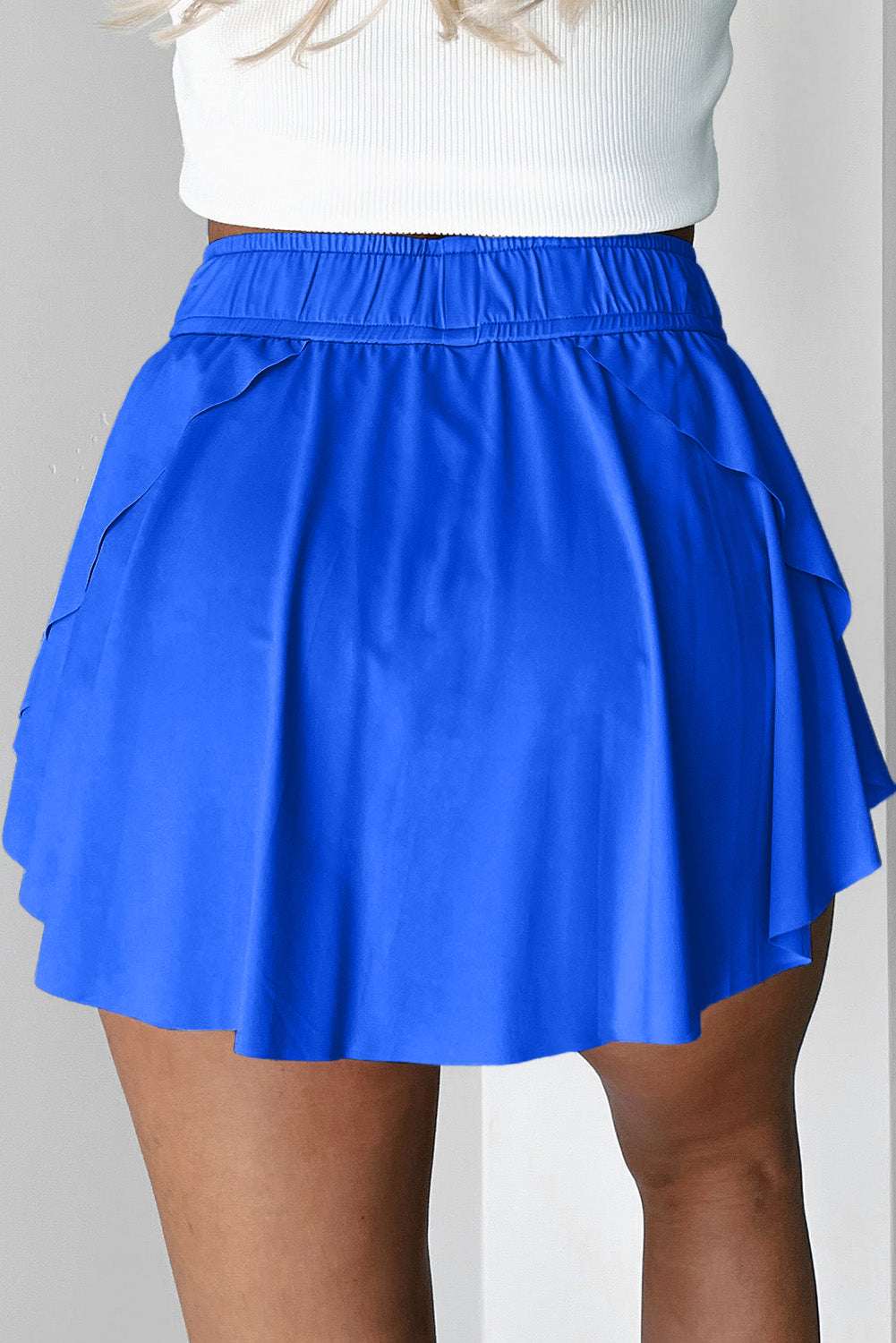 Blue fabric tennis skort with an elastic waistband and layered hem shown from the back.