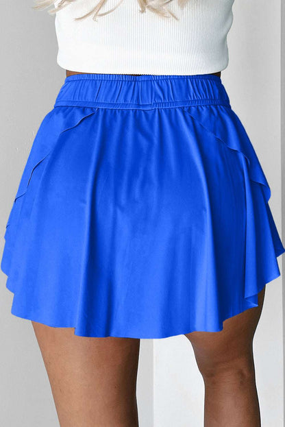 Blue fabric tennis skort with an elastic waistband and layered hem shown from the back.