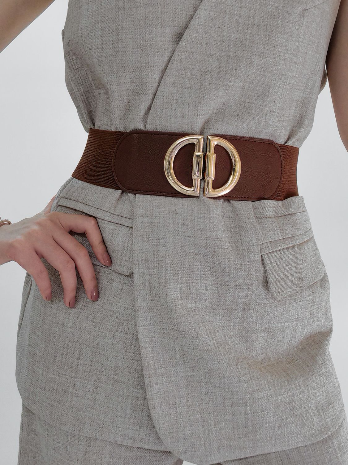 Person wearing a gray outfit with a brown belt and gold buckle on a plain background