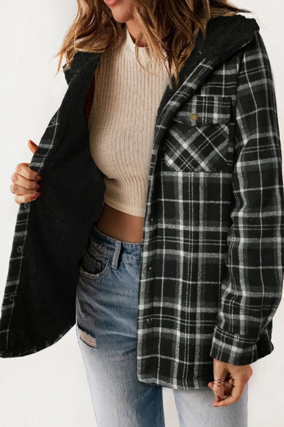 Person wearing a black and gray plaid jacket over a beige sweater and blue jeans on a white background