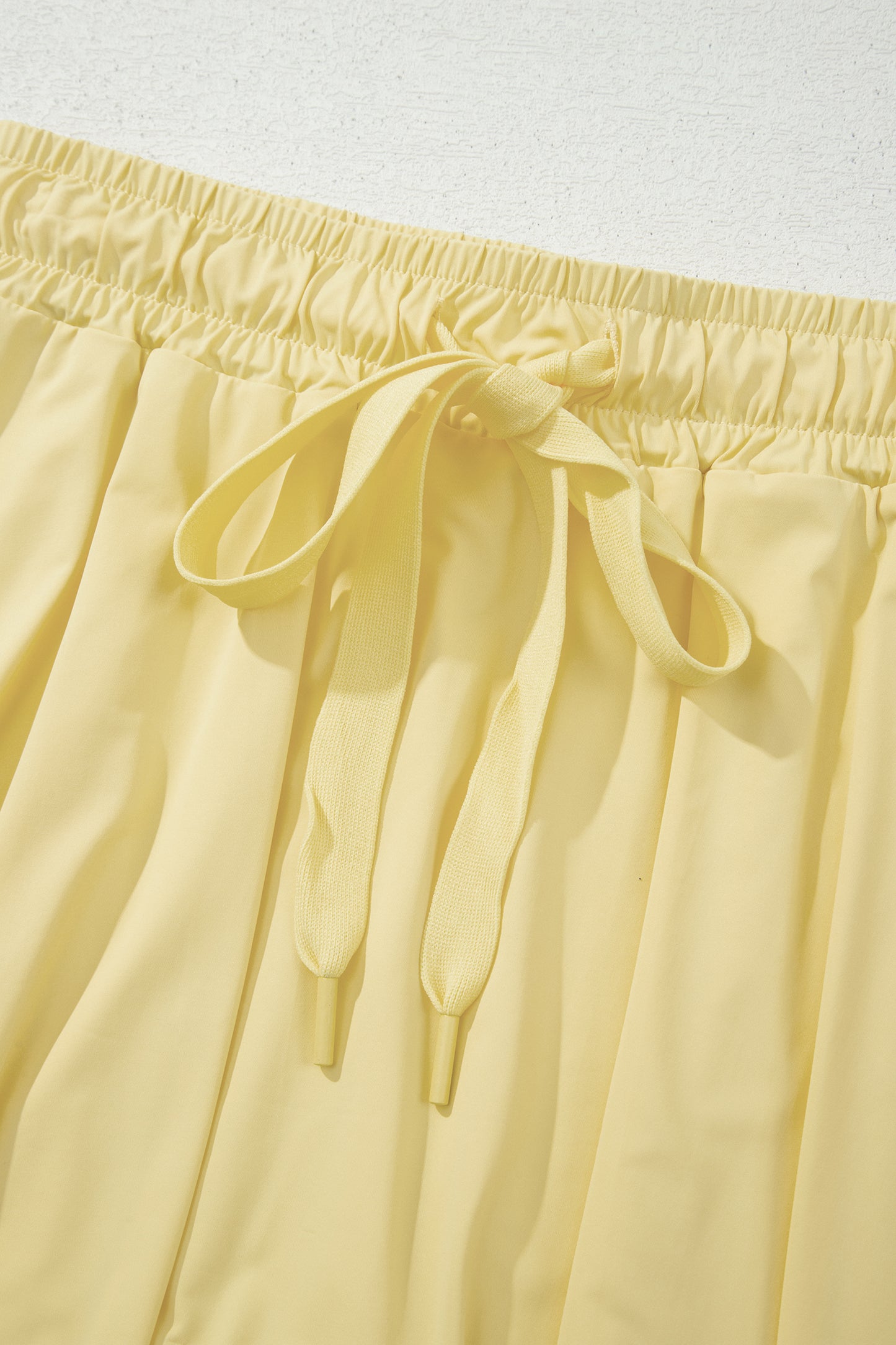 Close-up of pale yellow drawstring shorts showing the elastic waistband and tie detail.