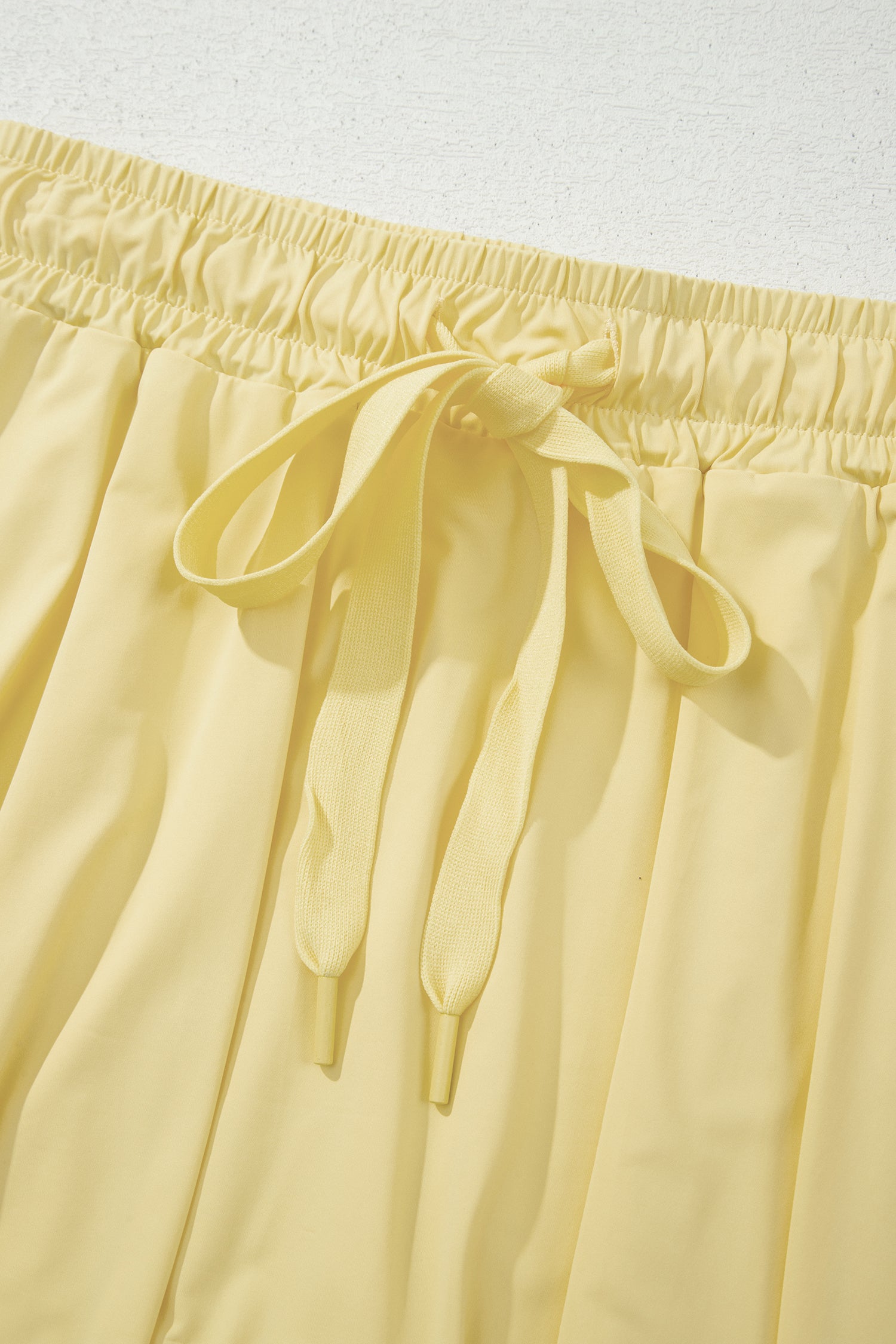 Close-up of pale yellow drawstring shorts showing the elastic waistband and tie detail.