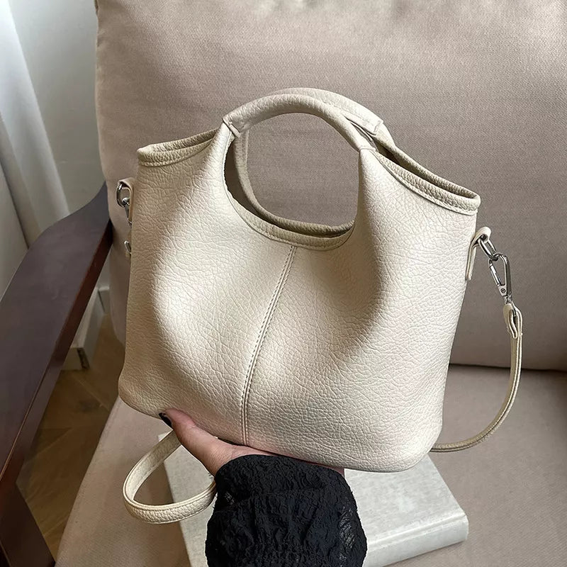Beige handbag held by a person with a neutral background