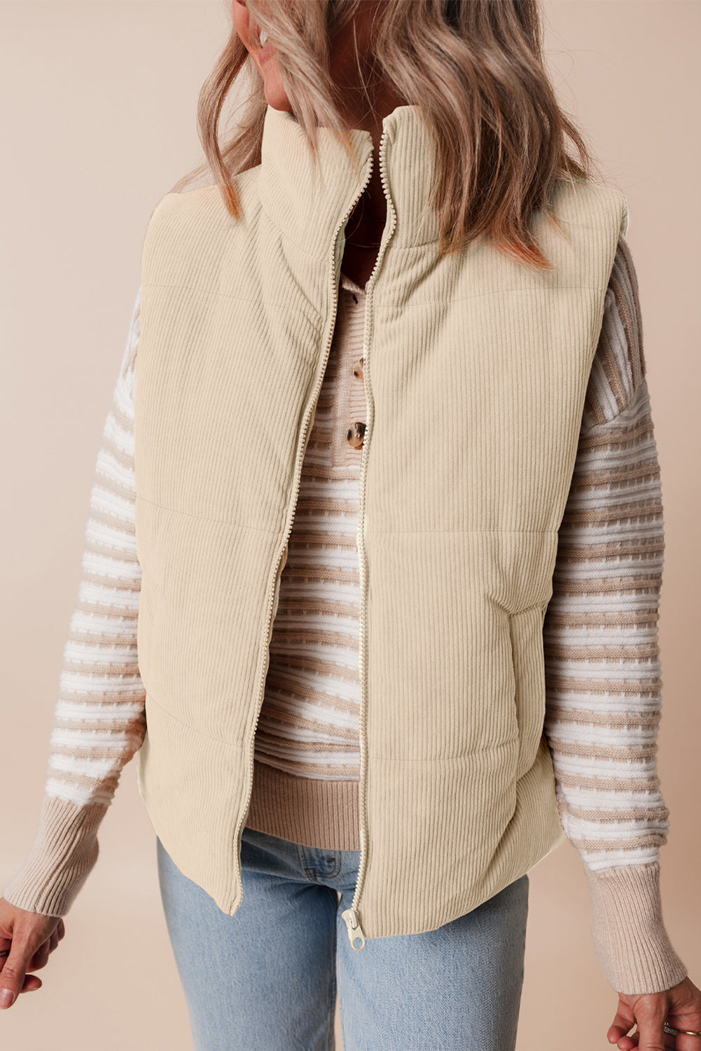 Person wearing a beige quilted vest over a striped sweater with a plain background