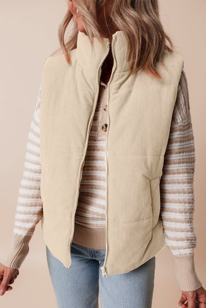 Person wearing a beige quilted vest over a striped sweater with a plain background