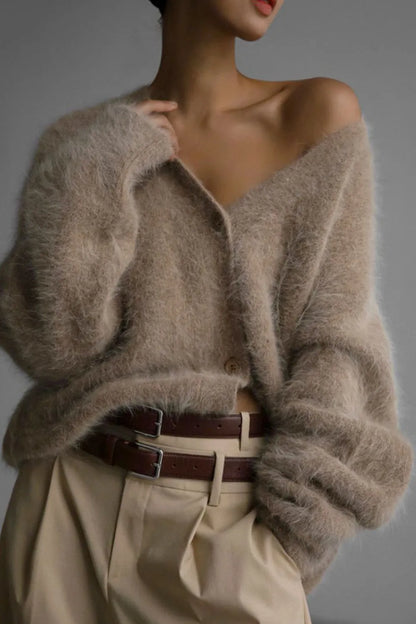 Person wearing a beige cardigan and beige pants with a brown belt against a gray background