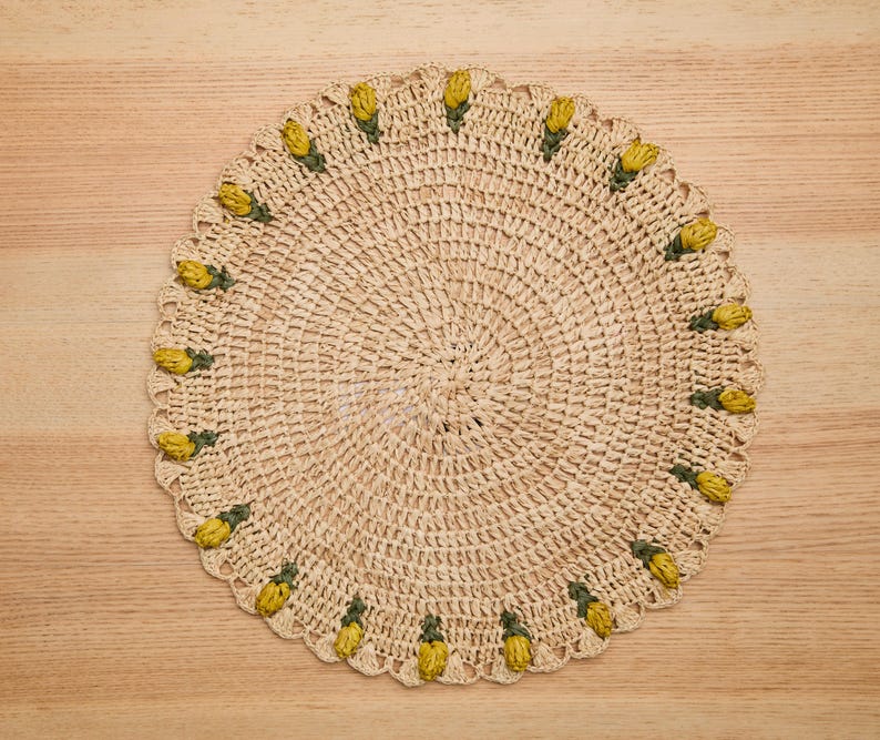 Round raffia crochet placemat featuring yellow tulip designs along the edge, set on a wooden surface.