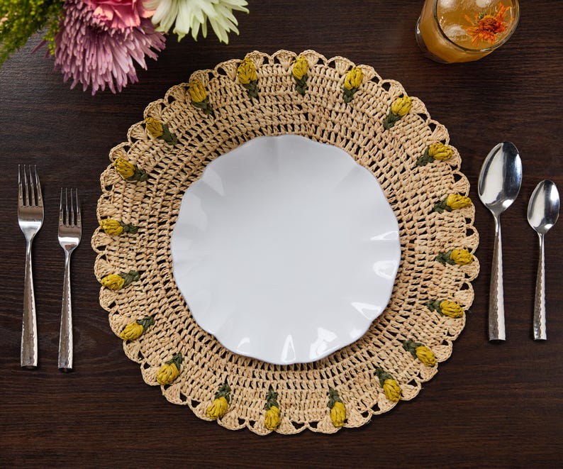 Handmade raffia crochet tulip placemat with yellow floral accents, featuring a white plate and silver cutlery on a wooden ...