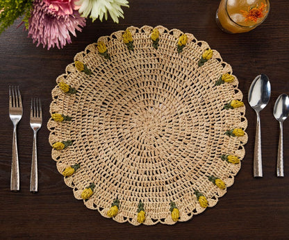 Handmade raffia crochet placemat with yellow tulip accents, set on a dark wooden table with utensils.