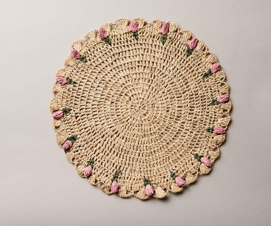 Hand-crocheted raffia palm placemat with pink tulip accents, round shape, ideal for spring table decor.