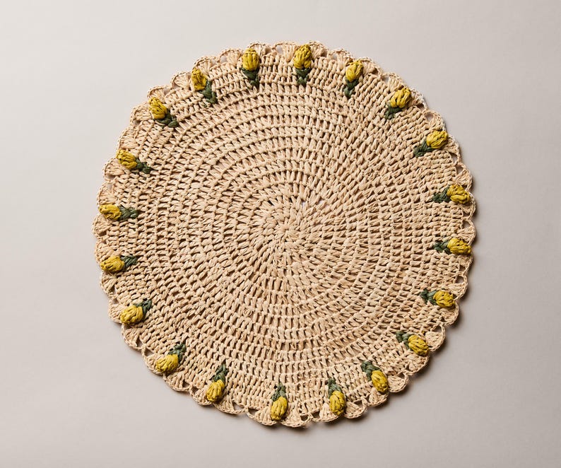 Handmade raffia crochet placemat featuring yellow tulip accents on a round, natural fiber design.