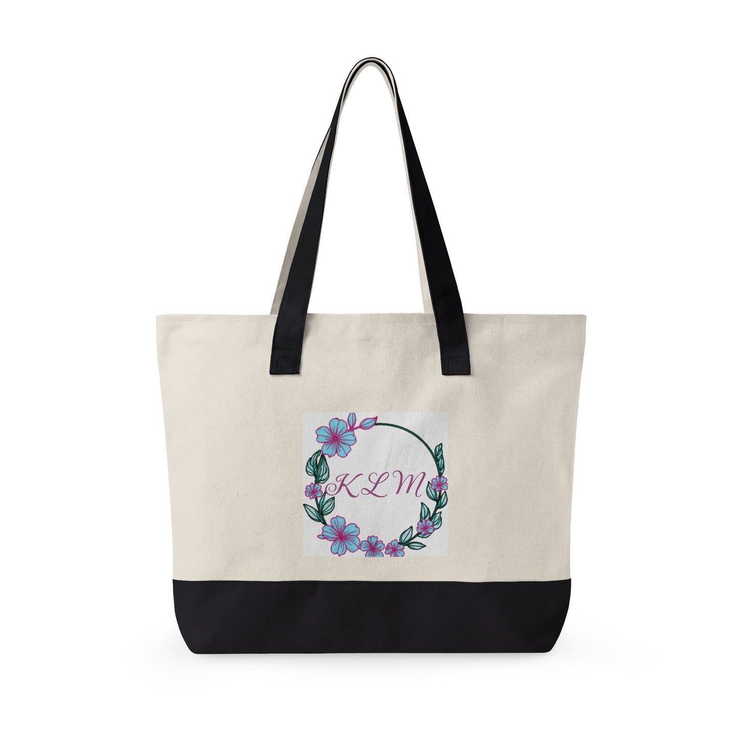 Cream and black fabric tote bag with black handles and a floral wreath design featuring the monogram KLM.