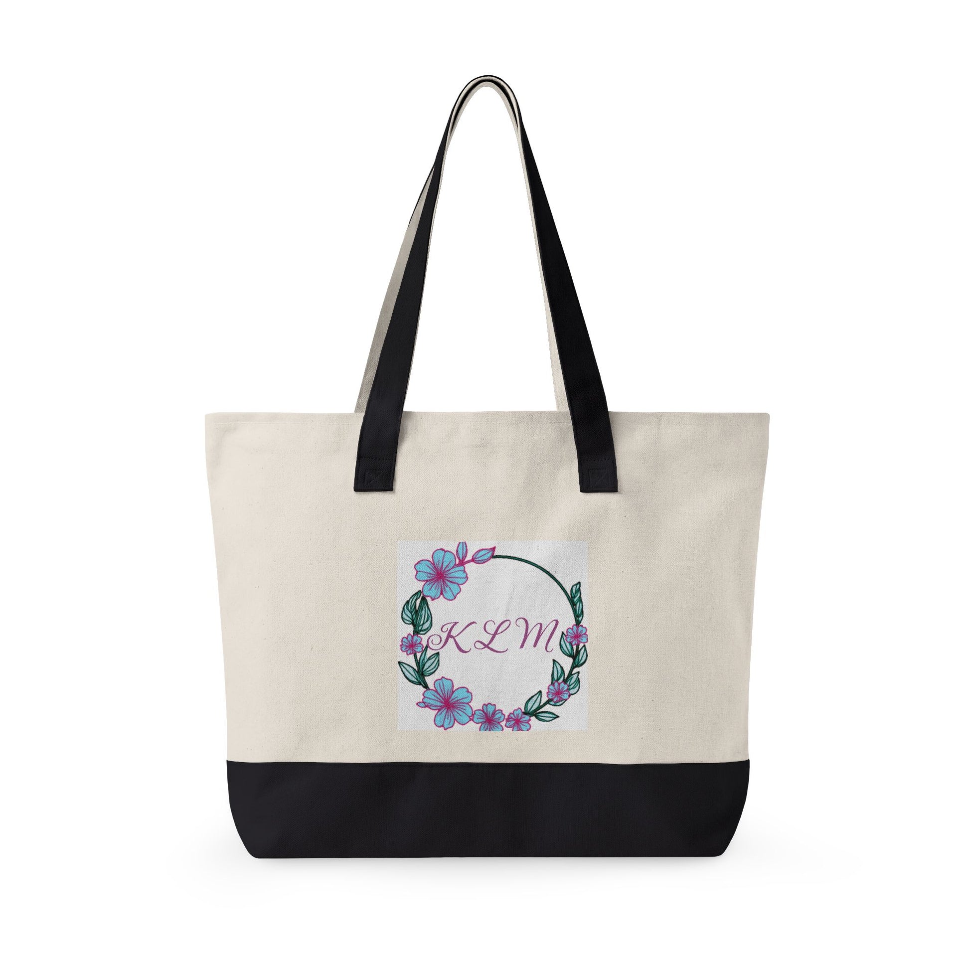 Cream and black fabric tote bag with black handles and a floral wreath design featuring the monogram KLM.