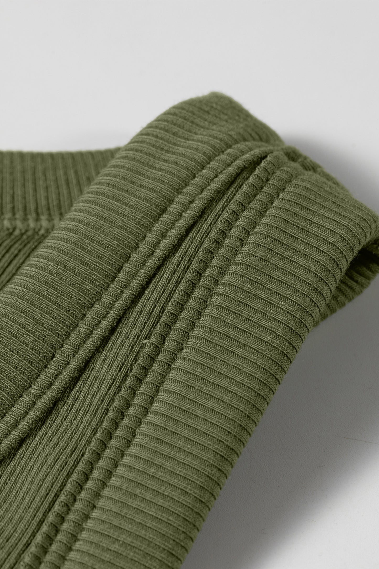 Close-up of a green ribbed sweater on a light gray background