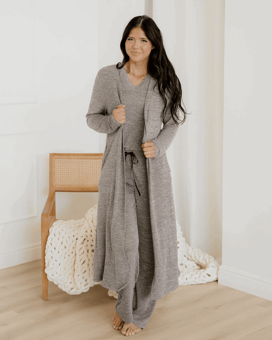 Woman wearing a long gray cardigan in a minimalistic room.