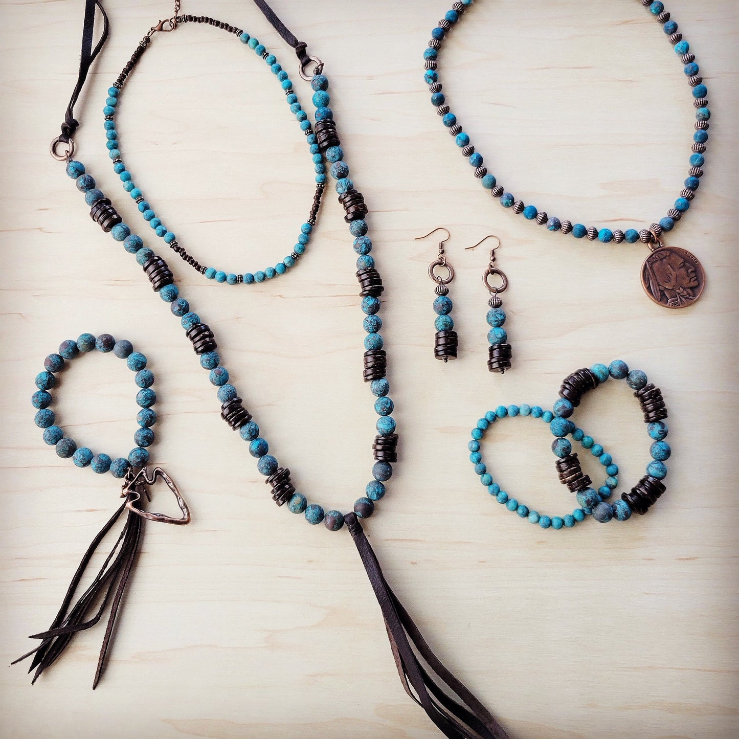 Jewelry set with blue and black beaded necklaces, bracelets, and earrings on a light wooden surface.