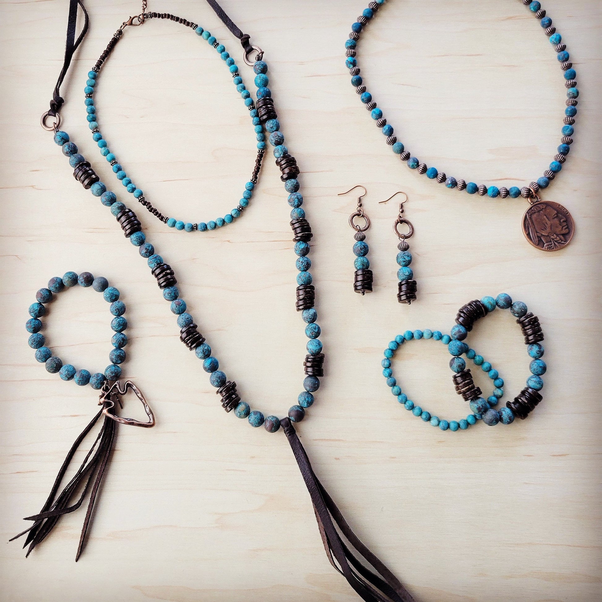 Jewelry set with blue and black beaded necklaces, bracelets, and earrings on a light wooden surface.