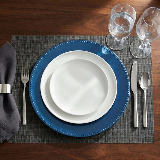 Dining table setting with blue plates, white bowls, silverware, and glasses on a wooden table.