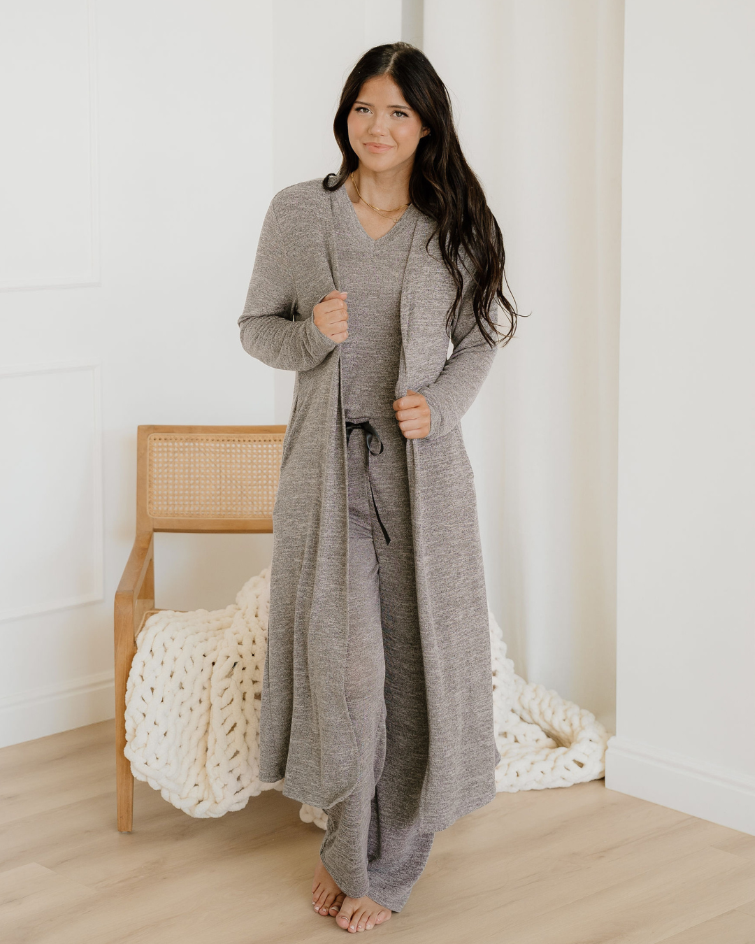 Woman wearing a long gray cardigan in a minimalistic room.