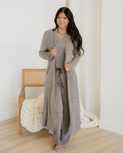 Woman wearing a long gray cardigan in a minimalistic room.
