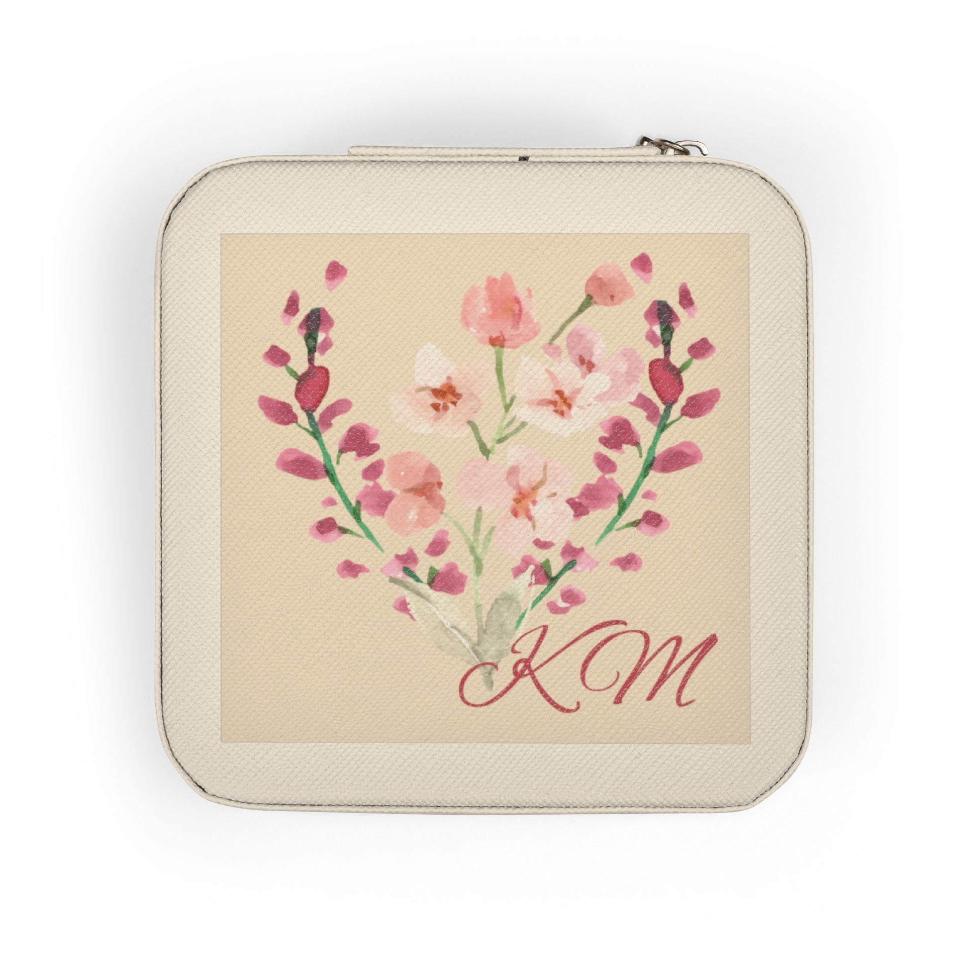 A square zippered pouch with rounded corners, featuring a cream-colored textured exterior and a central printed illustration of pink and white flowers arranged in a heart shape with the initials 'KM' in red script on a beige background.