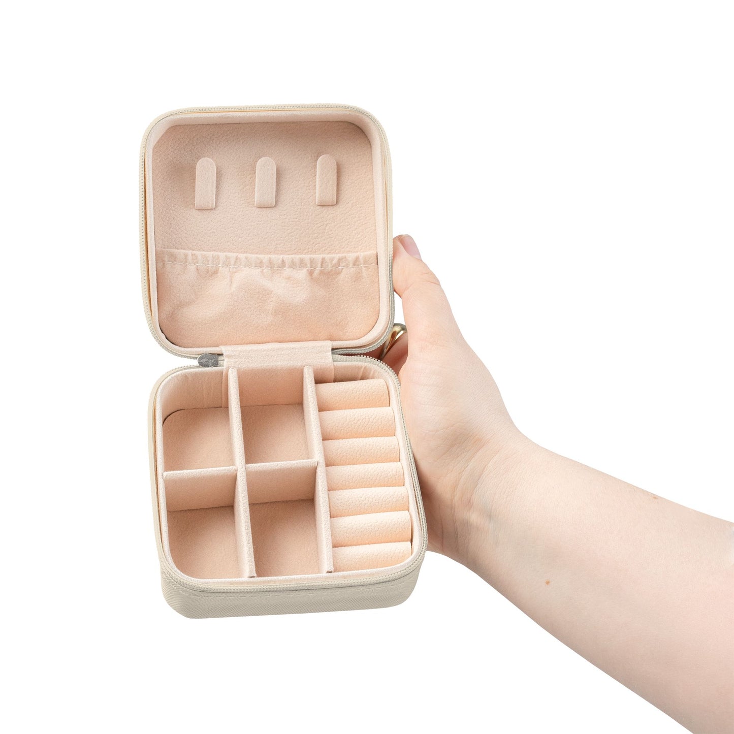 Beige jewelry case with compartments held open by a hand on a white background