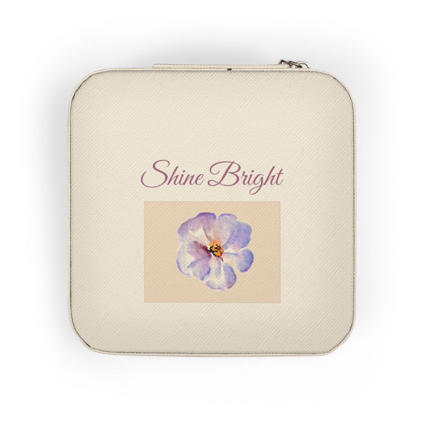 A square cream-colored zippered pouch with rounded corners, featuring the text 'Shine Bright' in a dusty rose script above a central square graphic of a purple and blue flower on a beige background.