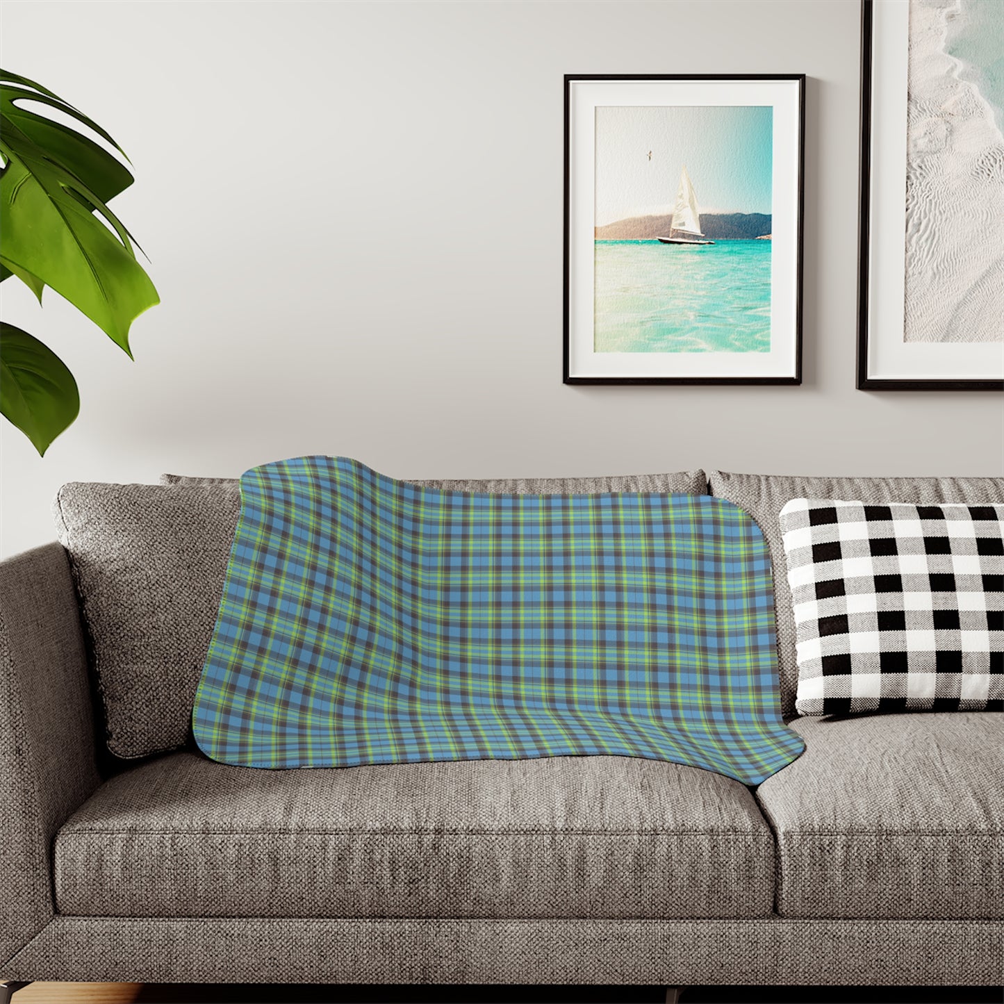 A plaid throw blanket in blue and green is draped over a gray fabric sofa in a living room setting, next to a black and white checkered pillow.