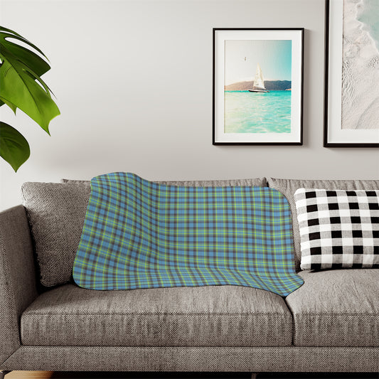 A plaid throw blanket in blue and green is draped over a gray fabric sofa in a living room setting, next to a black and white checkered pillow.