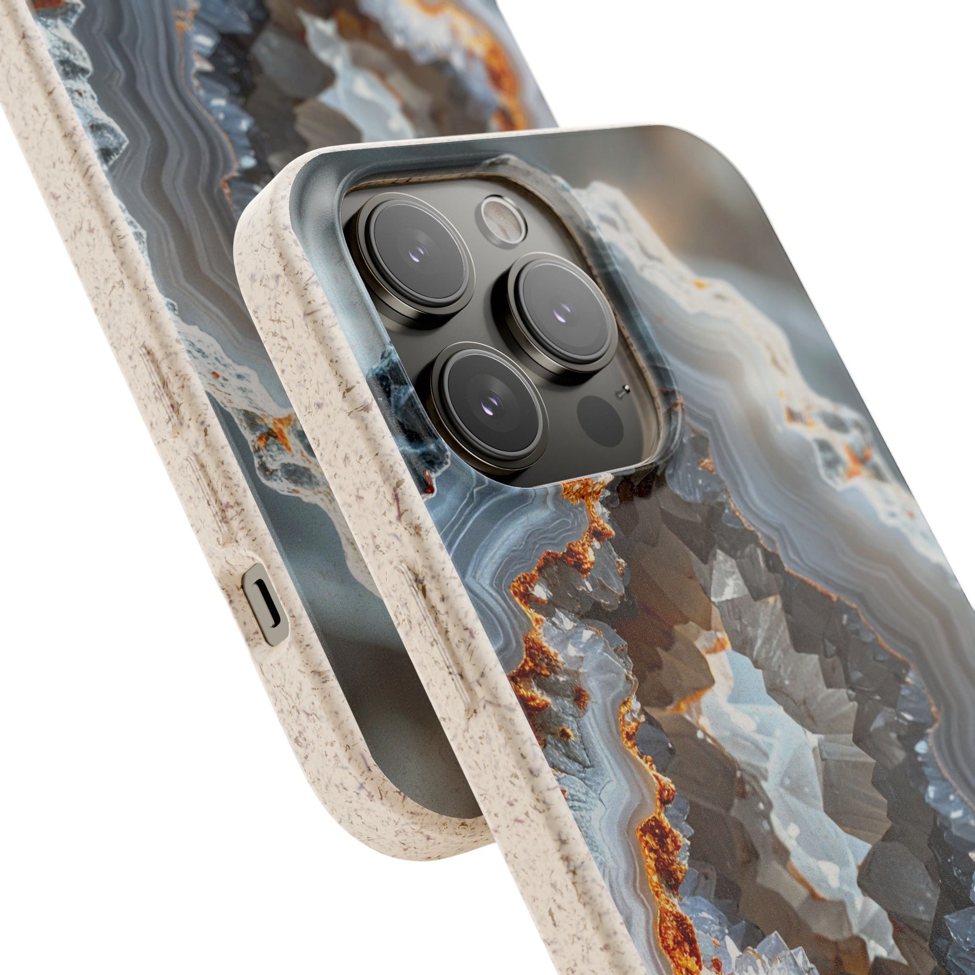 A close-up of a smartphone case with a geode-inspired agate pattern in gray, blue, white, and rust-orange tones, with a speckled beige bumper edge. The phone camera module is visible through a cutout in the back of the case.