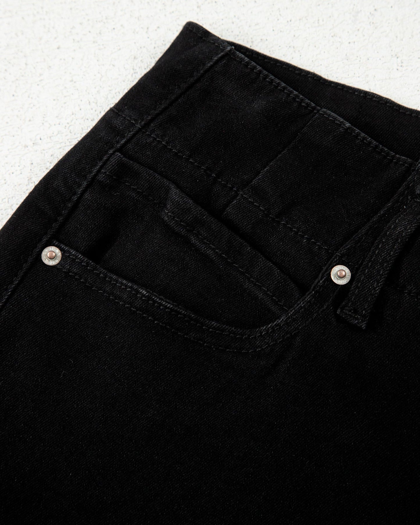 Close-up of black jeans with button details on a light gray background