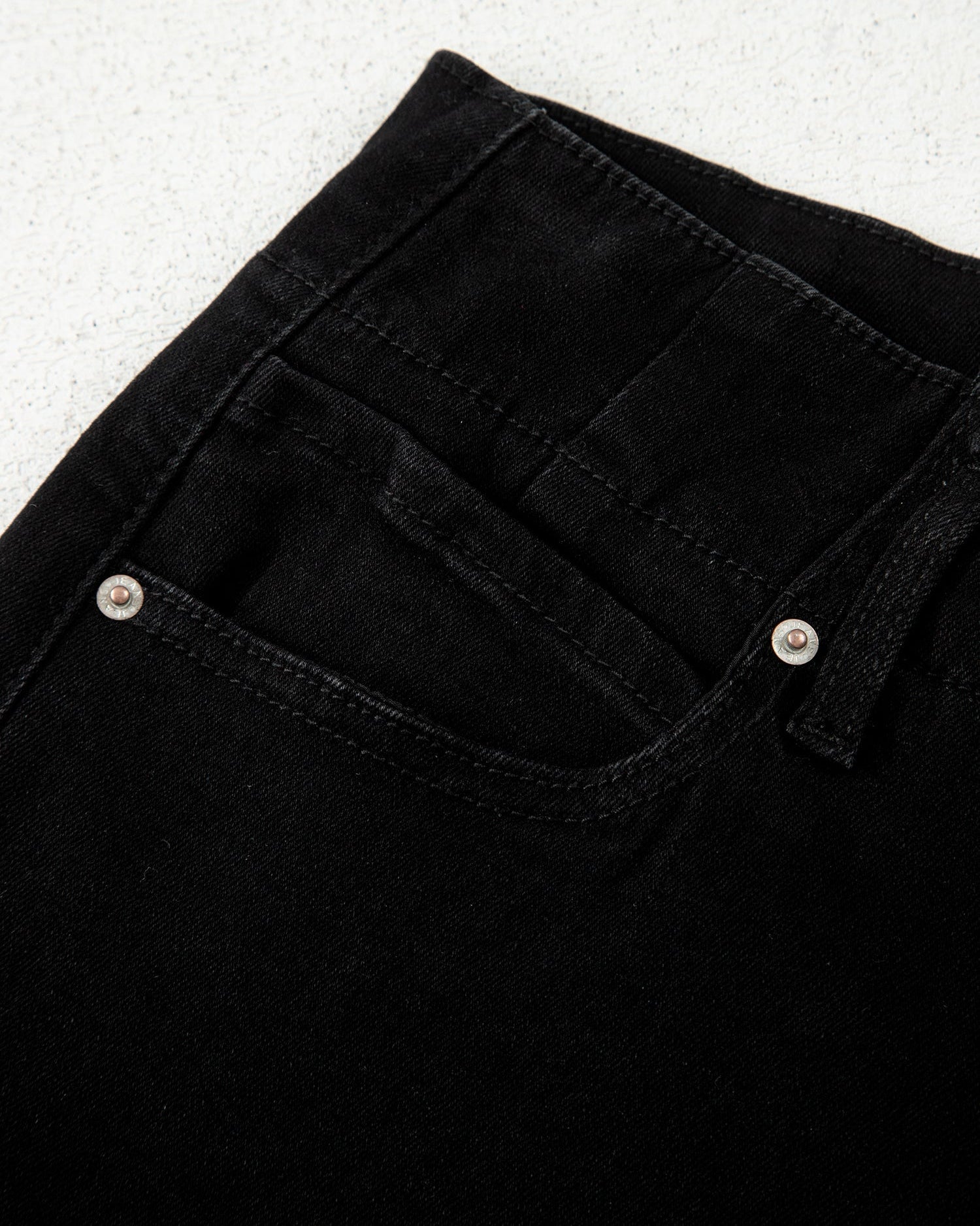 Close-up of black jeans with button details on a light gray background