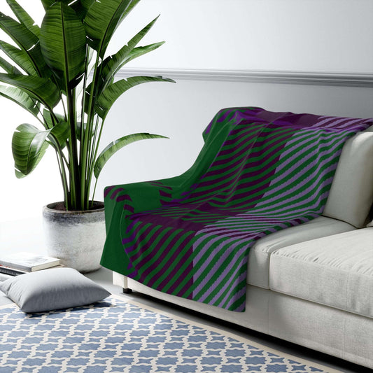 A throw blanket with a bold diagonal striped pattern in green and purple is draped over a light gray sofa in a modern living room setting next to a large potted plant.