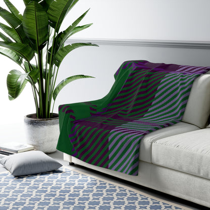 A throw blanket with a bold diagonal striped pattern in green, purple, and gray is draped over a light gray sofa in a modern living room setting next to a large potted plant.