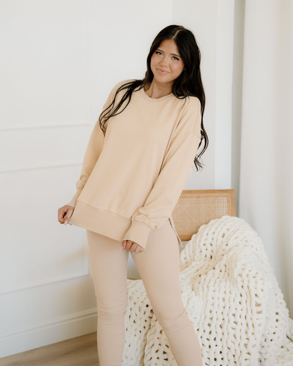 Woman wearing a beige outfit sitting on a white surface with a white wall background