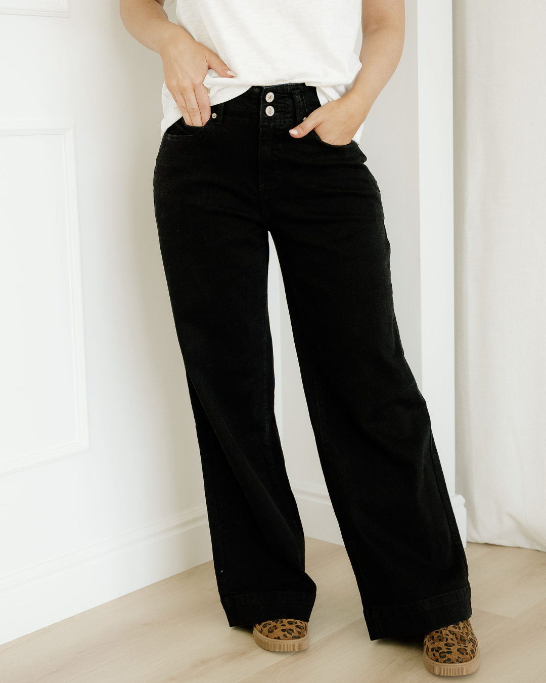 Person wearing black wide-leg jeans and a white top against a white background