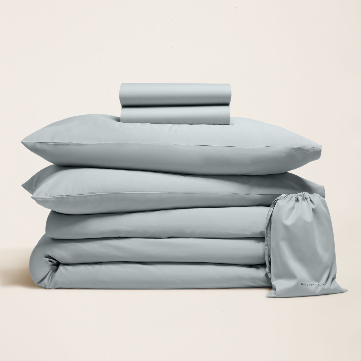 Stack of light blue bedding set with a drawstring bag on a beige background