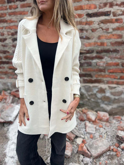 Model wearing a white double-breasted coat with cable-knit sleeves, buckled cuffs, wide lapels and front pockets.
