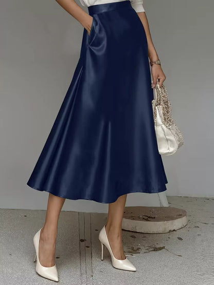 Person wearing a navy blue satin skirt with white high-heeled shoes on a neutral background