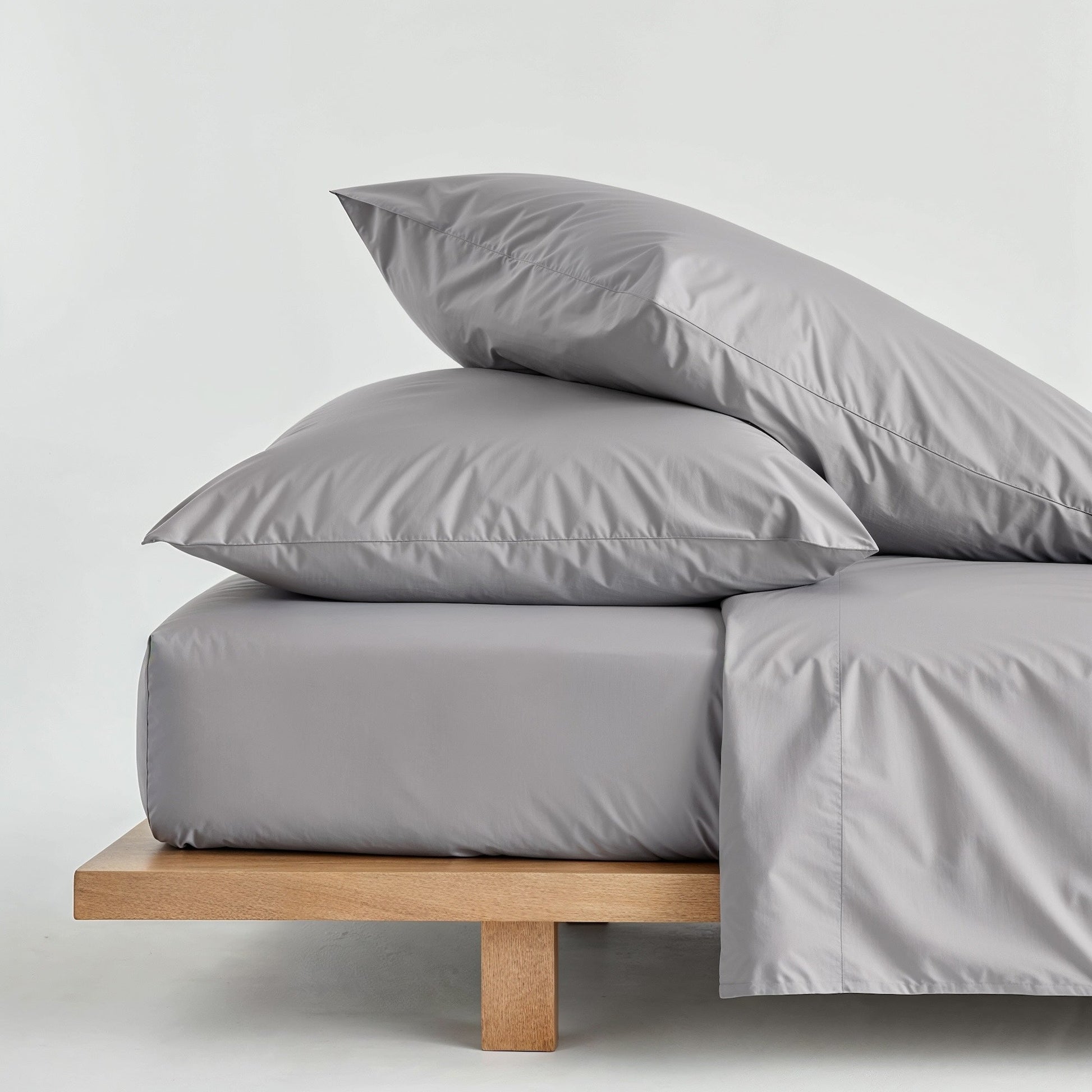 Gray bedding set with pillows on a wooden bed frame against a light gray background