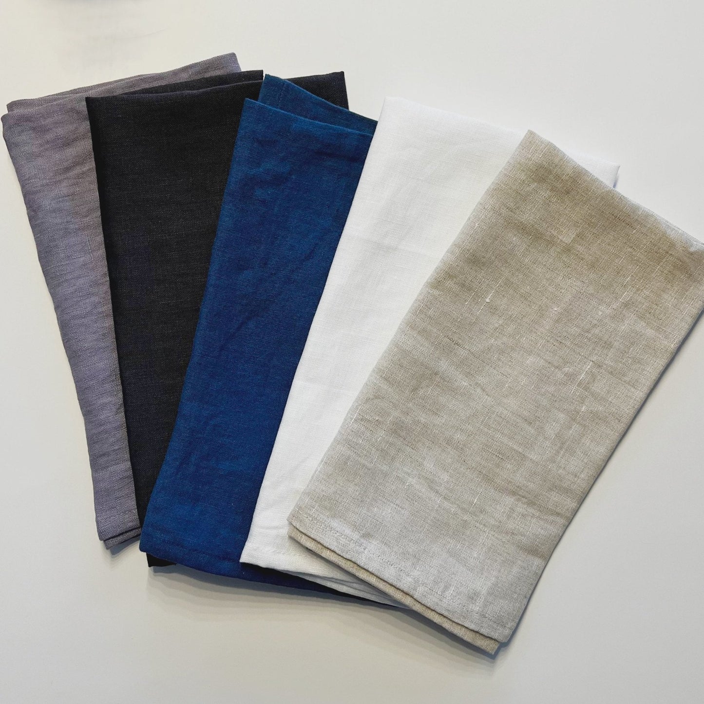 Five folded fabric swatches in gray, black, blue, white, and beige on a light gray background