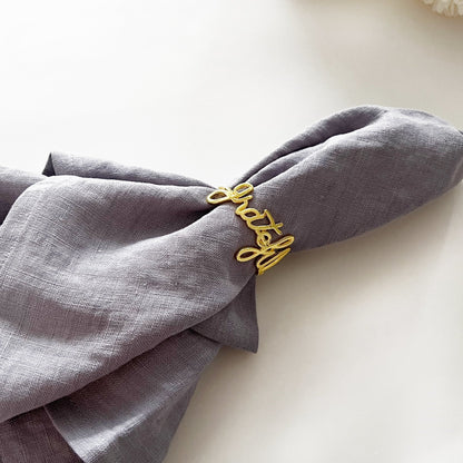 Gray napkin with a gold 'Lucky' napkin ring on a light background