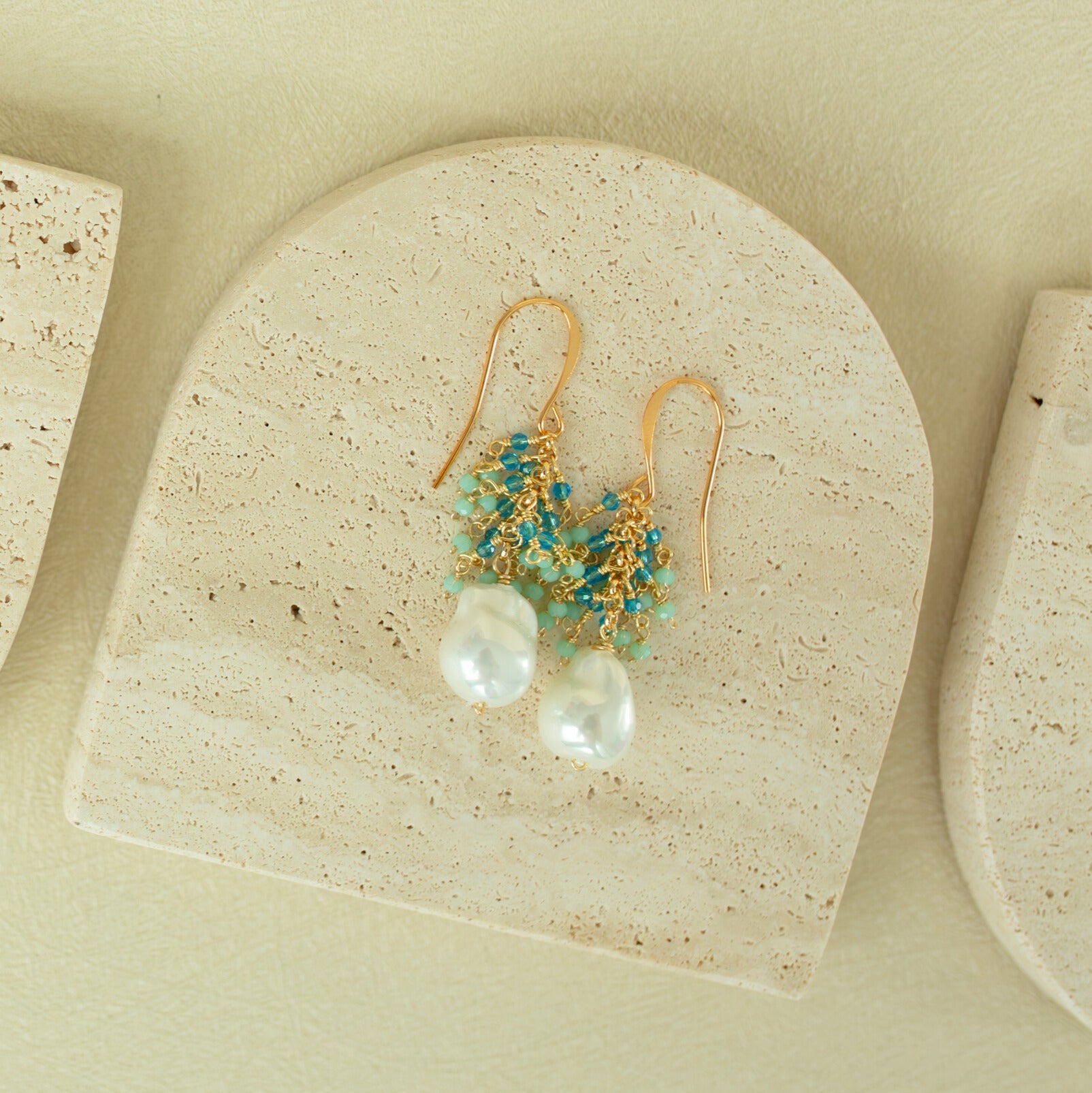 Gold earrings with pearls and turquoise beads on a beige stone surface