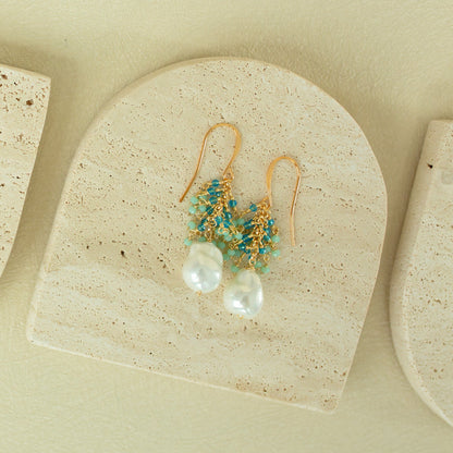 Gold earrings with pearls and turquoise beads on a beige stone surface