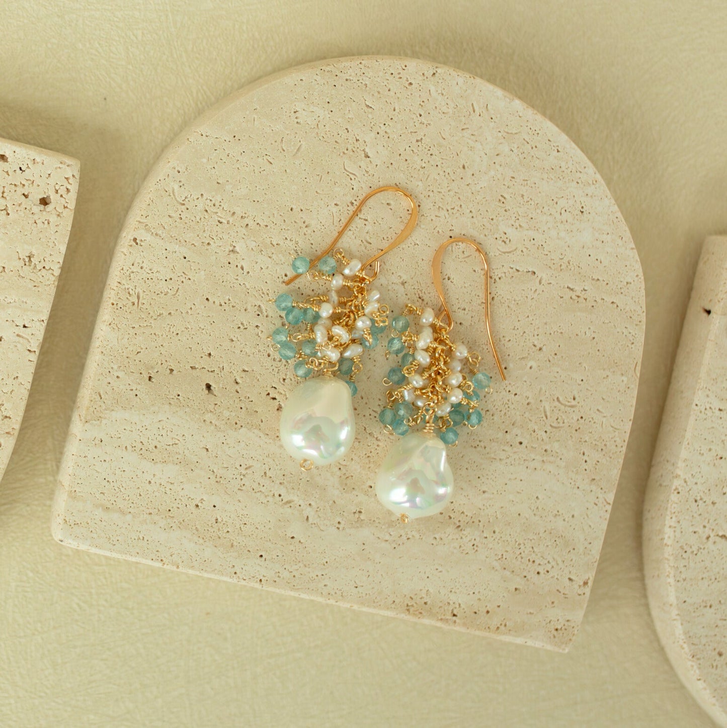 Pair of gold earrings with pearls and turquoise beads on a beige stone surface