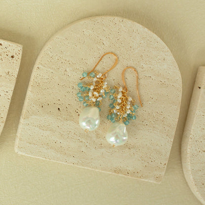 Pair of gold earrings with pearls and turquoise beads on a beige stone surface