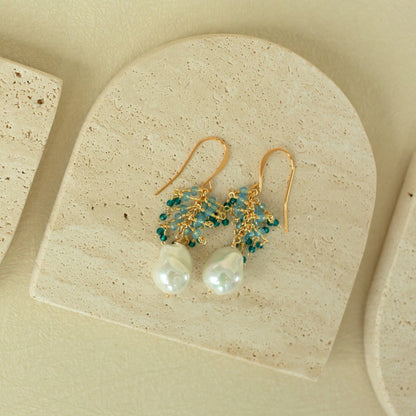 Gold earrings with pearls and green beads on a beige stone surface