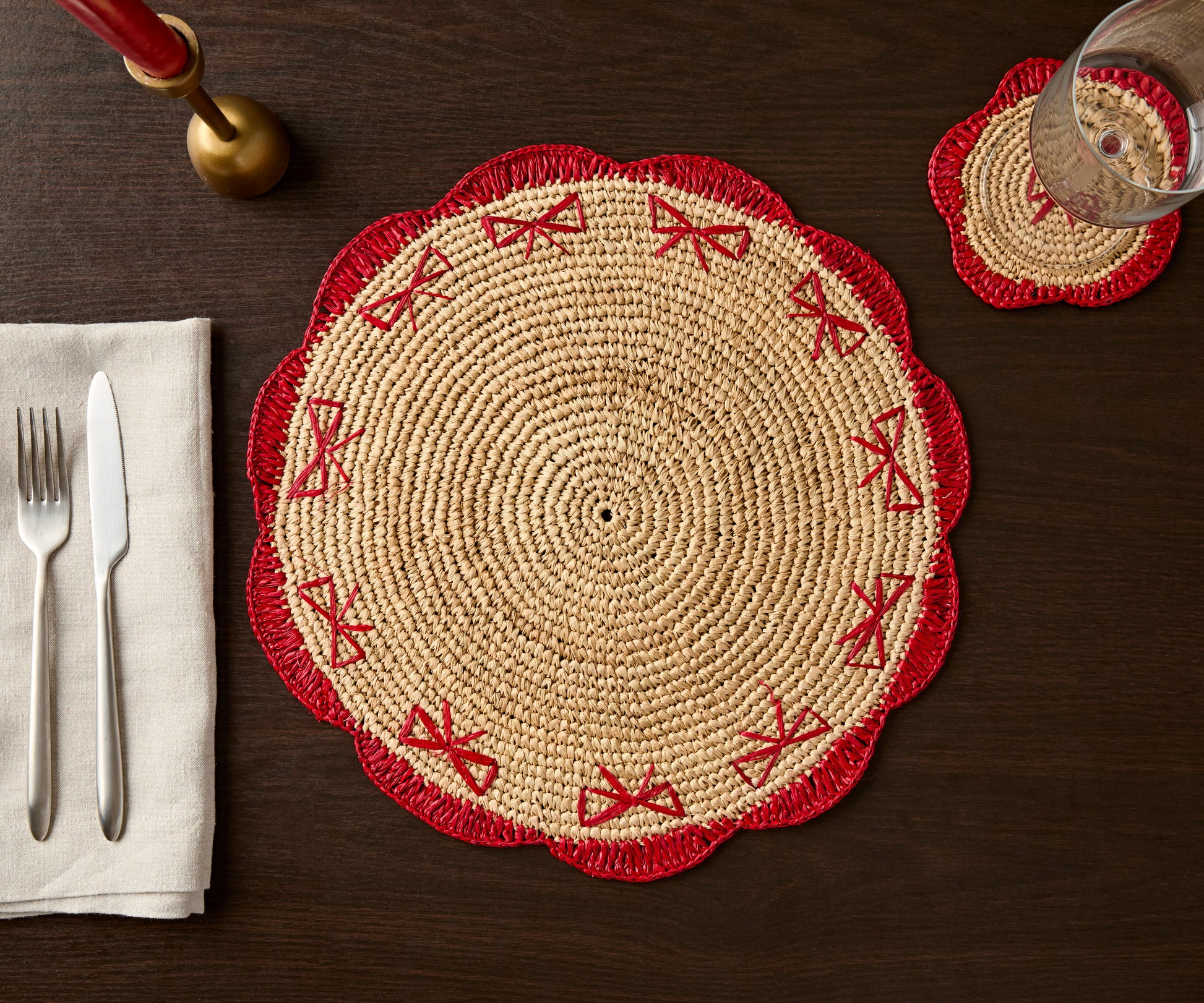 Handwoven raffia fringe coaster with red scalloped edges and bow designs on a dark wooden table setting.